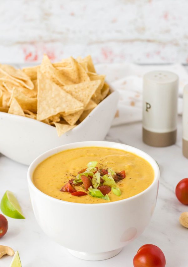 Vegan queso in a bowl with chips behind it.