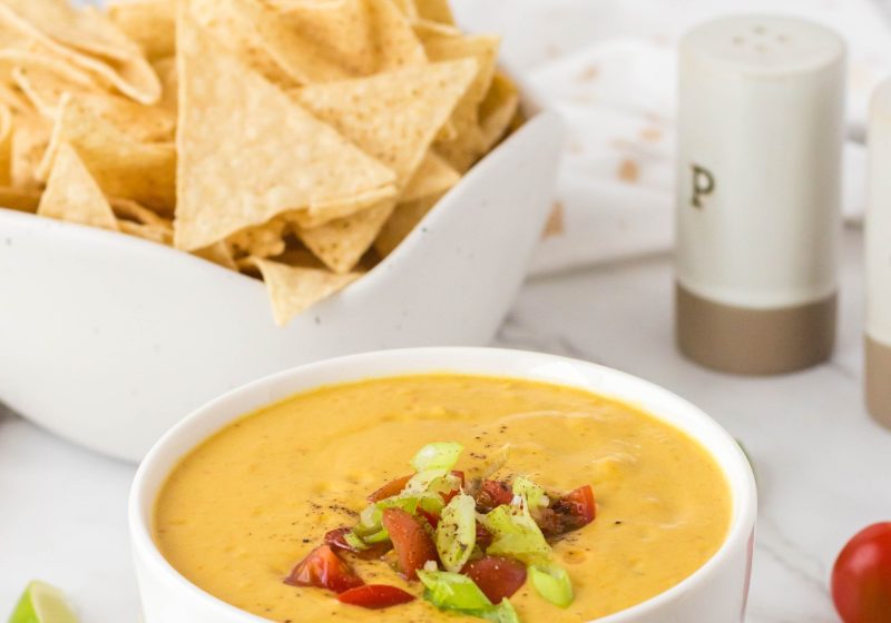 Vegan queso in a bowl with chips behind it.