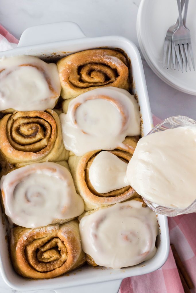 Baked vegan cinnamon rolls being topped with cream cheese frosting