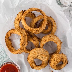 A pile of onion rings on a piece of parchment with a side of ketchup.