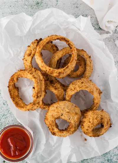 A pile of onion rings on a piece of parchment with a side of ketchup.