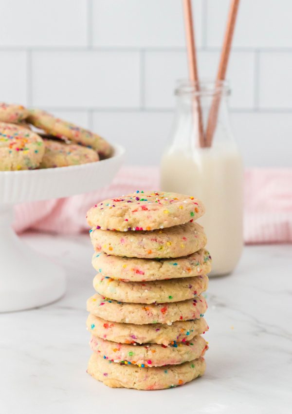 A stack of 8 cookies on a counter with a glass of milk in the background