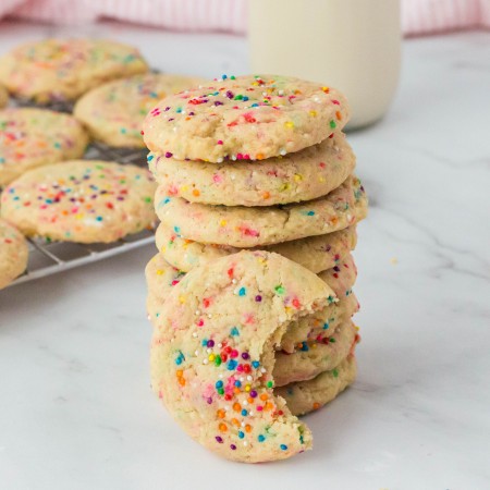 A stack of vegan funfetti cookies on a counter with one with a bite taken out for you to see.