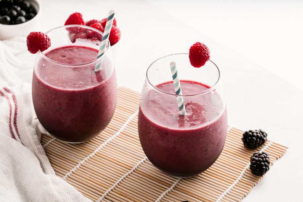 2 mixed berry smoothies with straws on a mat.