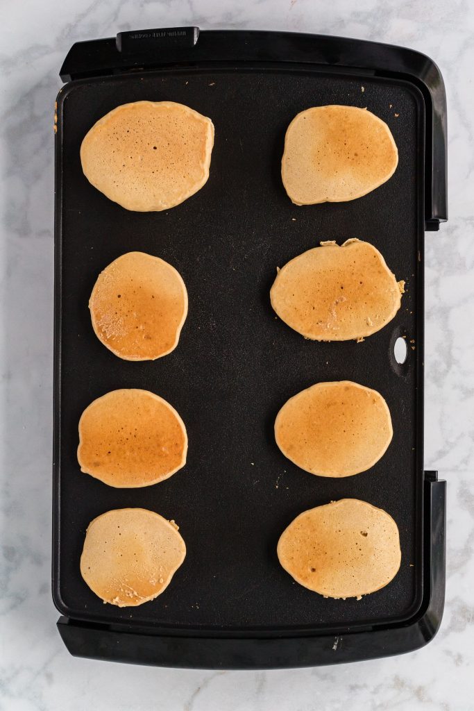 8 golden brown pancakes on a griddle.