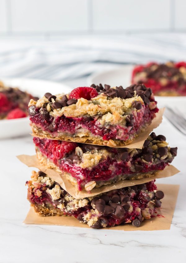 Vegan raspberry oatmeal bars stacked with parchment in between.