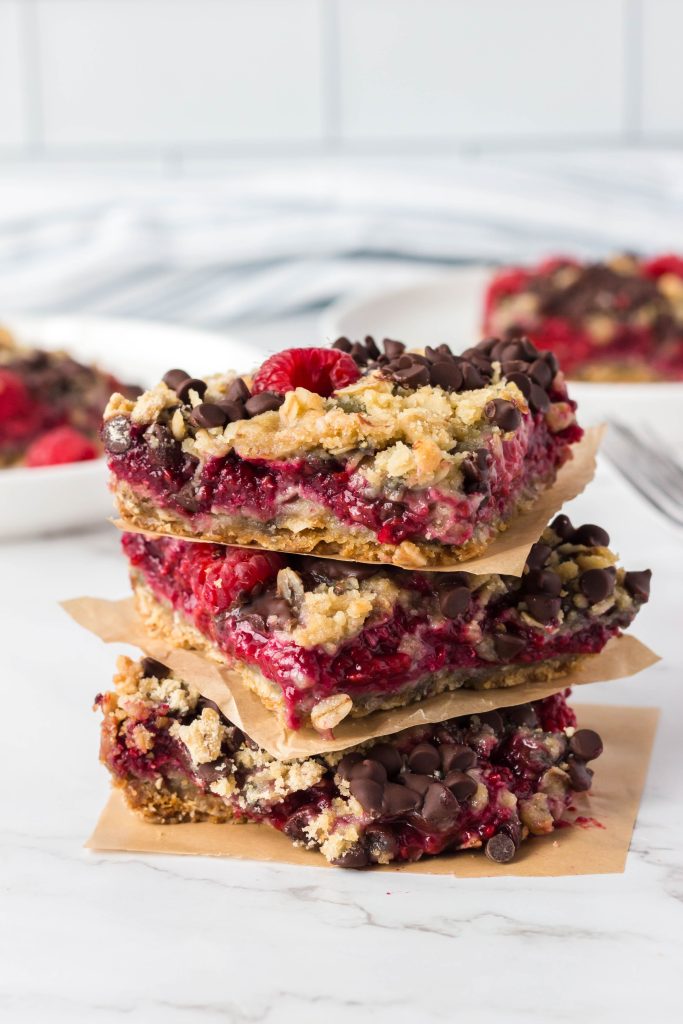 Vegan raspberry oatmeal bars stacked with parchment in between.