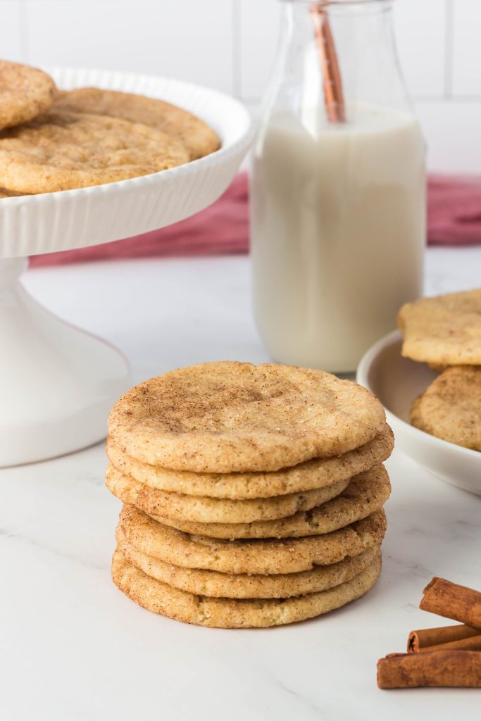 A stack of vegan snickerdoodle cookies on a counter with a glass of vegan milk behind it.