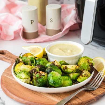Vegan air fryer brussels sprouts on a plate with dipping sauce.