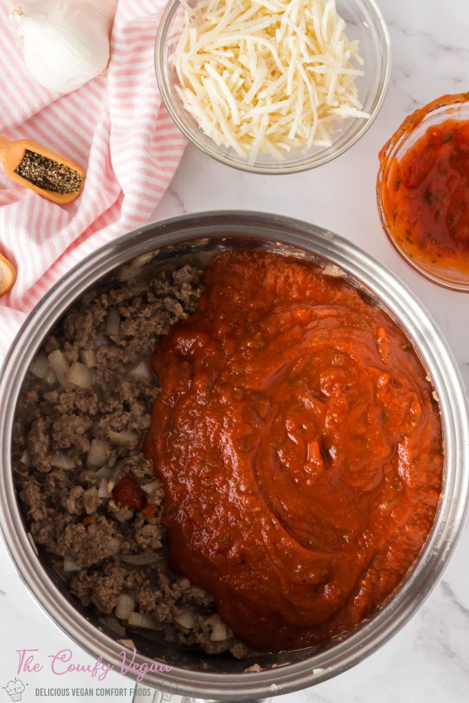 Marinara sauce is added to the vegan impossible meat mixture in a saucepan.