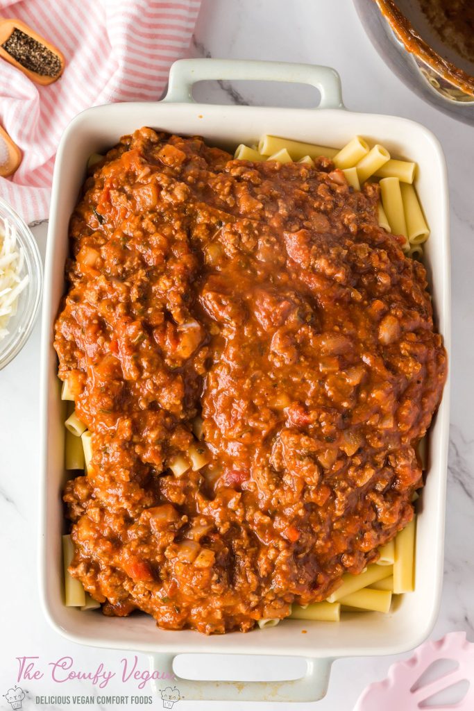 Pasta and the prepared marinara mixture is added to a casserole dish.