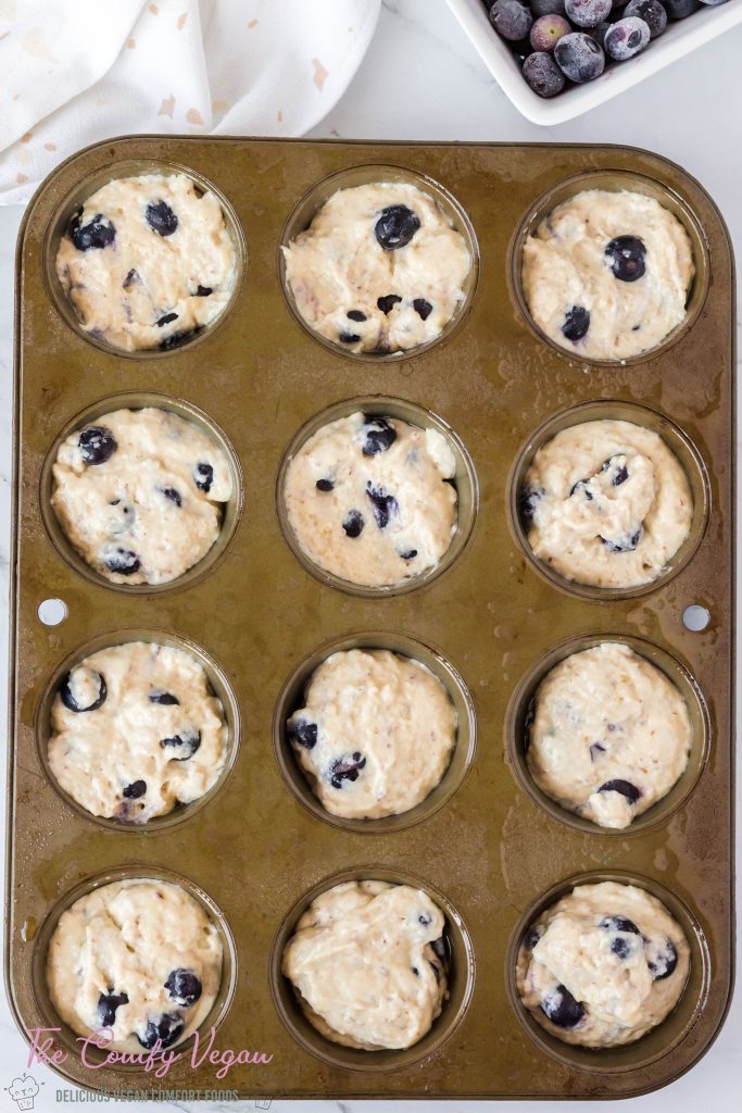 Blueberry batter added to a muffin pan.